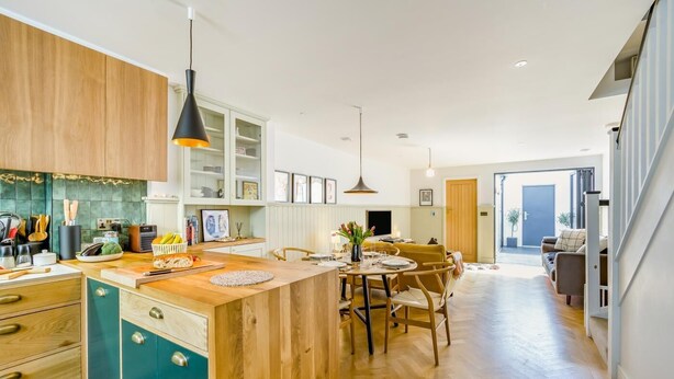 Eine moderne Küche mit Holzschränken, einer zentralen Kochinsel und einem Essbereich mit Tisch und Stühlen.