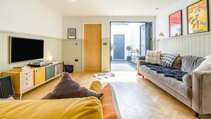 Ein modernes Wohnzimmer mit Flachbildfernseher, Sofa und einem kleinen Tisch mit Büchern.