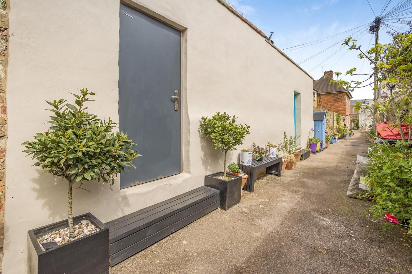 A narrow alleyway with a row of potted plants and a door on the left.