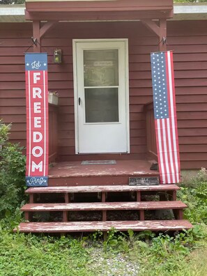 Eine Veranda mit einer weißen Tür, einem roten Banner mit der Aufschrift 'FREEDOM' und einer amerikanischen Flagge.