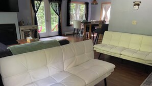 A living room with a white sofa, a dining table with chairs, and a view through a glass door. - 2bedroom home, lake access, snowmobile trail access, ac/fire place,  Indian Lake (Indian lake)