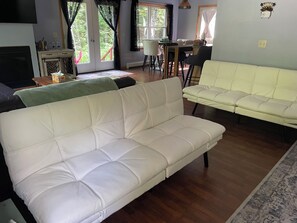 A living room with a white sofa, a dining table with chairs, and a view through a glass door. - 2bedroom home, lake access, snowmobile trail access, ac/fire place,  Indian Lake (Indian lake)