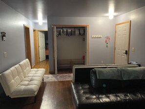 A room with a white sofa, a black leather couch, a wooden bench, and a door with a coat rack. - 2bedroom home, lake access, snowmobile trail access, ac/fire place, Indian Lake (Indian lake)
