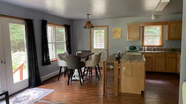 A spacious kitchen with wooden cabinets, a dining area with chairs, and a large window providing a view of the outdoors. - 2bedroom home, lake access, snowmobile trail access, ac/fire place,  Indian Lake (Indian lake)