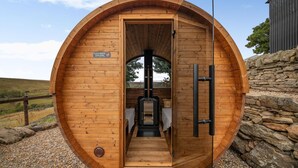 Een houten sauna met een bordje waarop staat schoenen uit te trekken, een glazen deur en een stenen muur op de achtergrond.