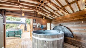 Een houten blokhut van binnen met een jacuzzi, houten balken en een bank buiten.