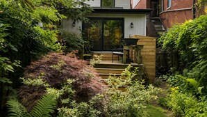 Une maison moderne dotée d’une terrasse, entourée d’une végétation luxuriante et d’un mur de briques.