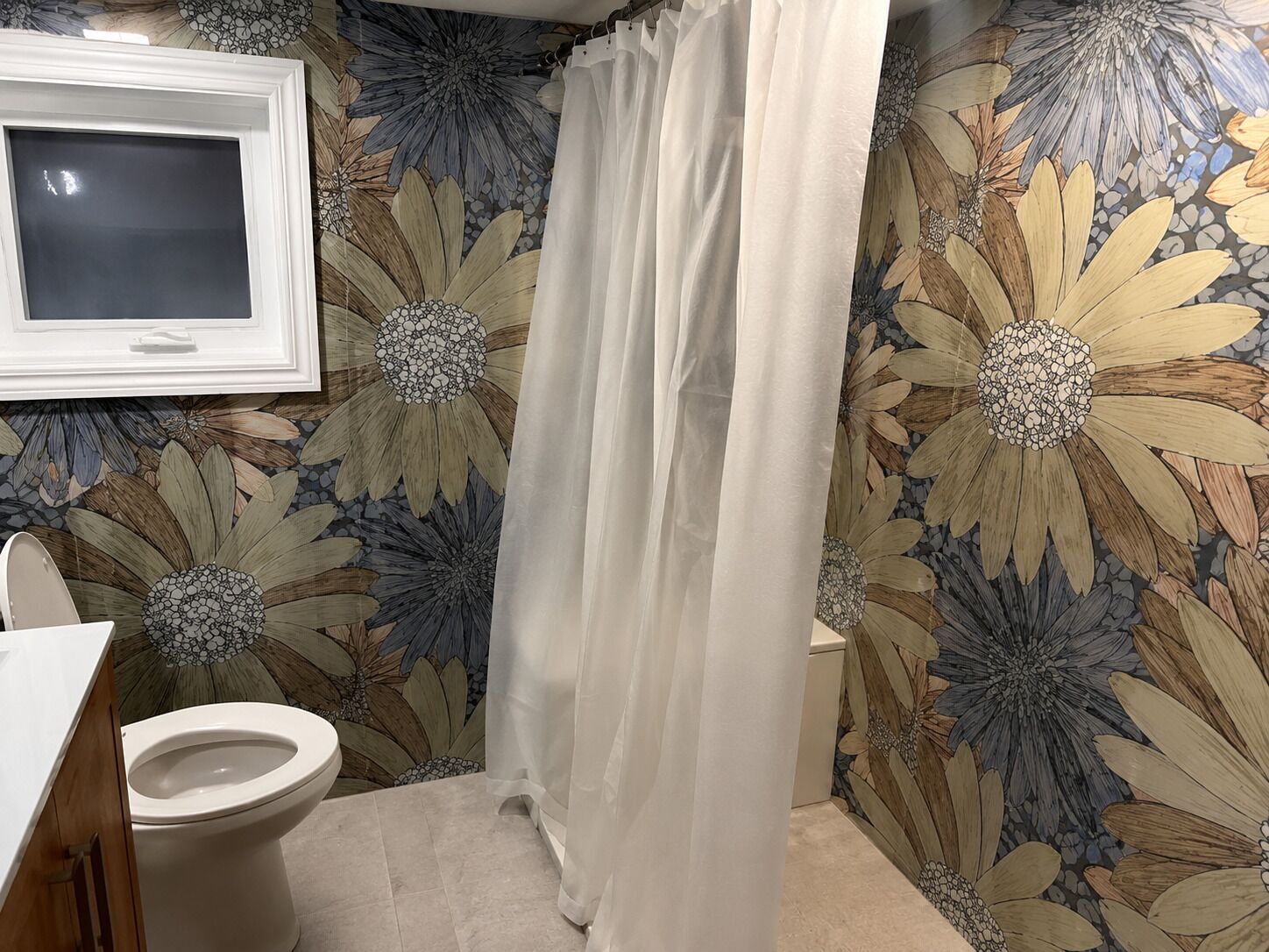 A bathroom with a toilet, a shower curtain, and a wall with a floral pattern.
