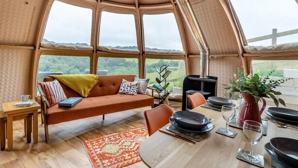 Ein gemütliches Interieur mit einer Couch, einem Esstisch und Blick durch große Fenster.