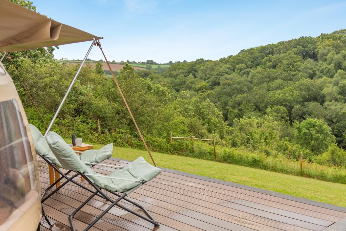 A wooden deck with a swing chair and a table, overlooking a lush green landscape.