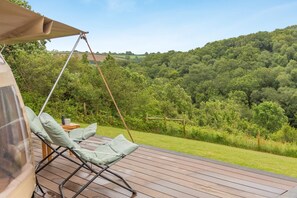A wooden deck with a swing chair and a table, overlooking a lush green landscape. - 1 Bed in Duloe (oc-w42785) (Duloe)