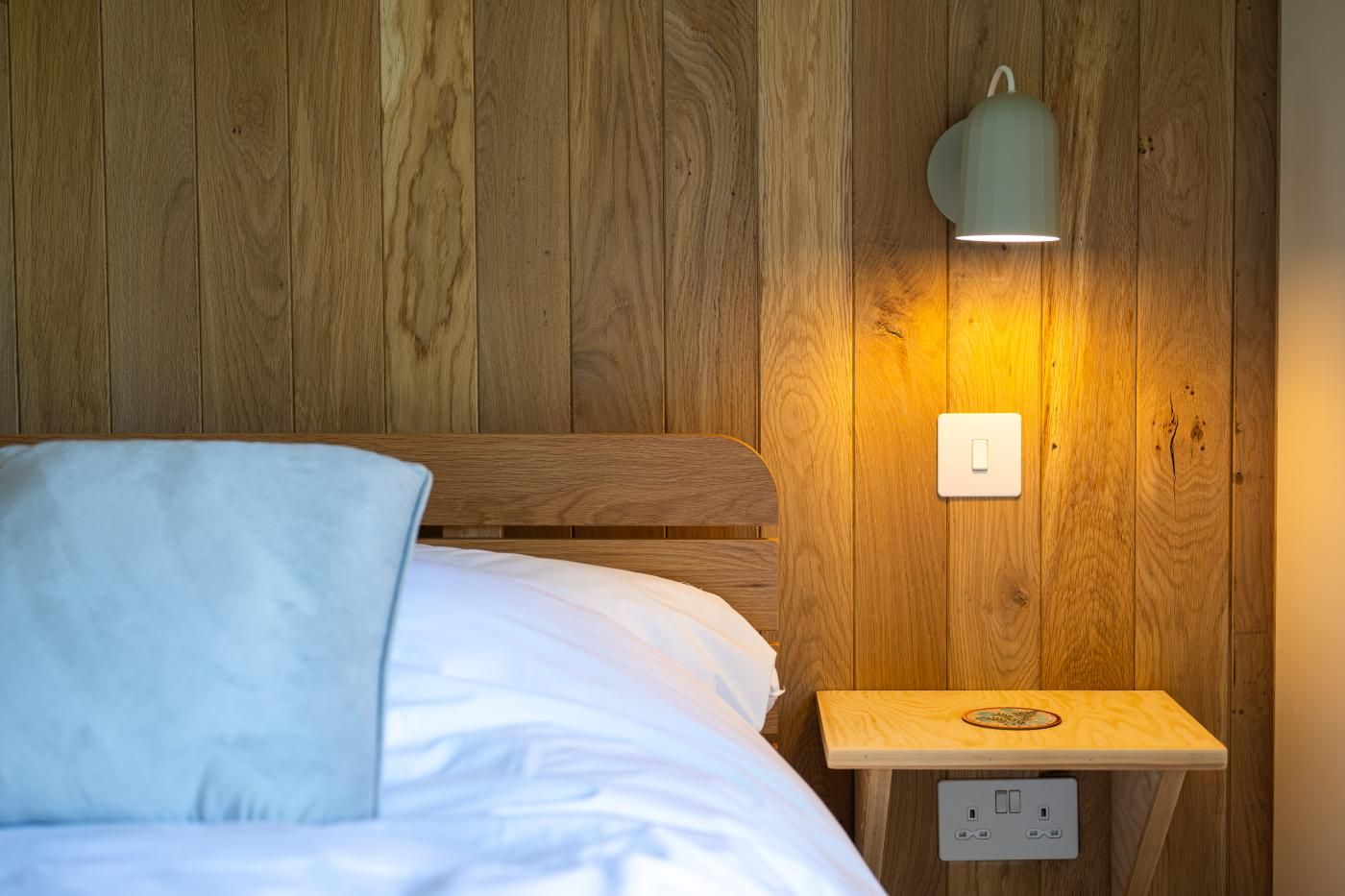 Pared de madera con una cama y una mesita de noche.
