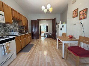 A kitchen with wooden cabinets, a stove, and a dining area with a table and chairs. - Cozy 1-bedroom apartment in charming Boston with high ceilings and bay windows (Boston)