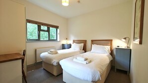 Une chambre avec deux lits, un bureau, une chaise, une fenêtre et un radiateur.