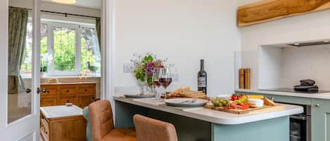 A kitchen with a dining area, wooden cabinets, a central island with food, and a window with curtains.