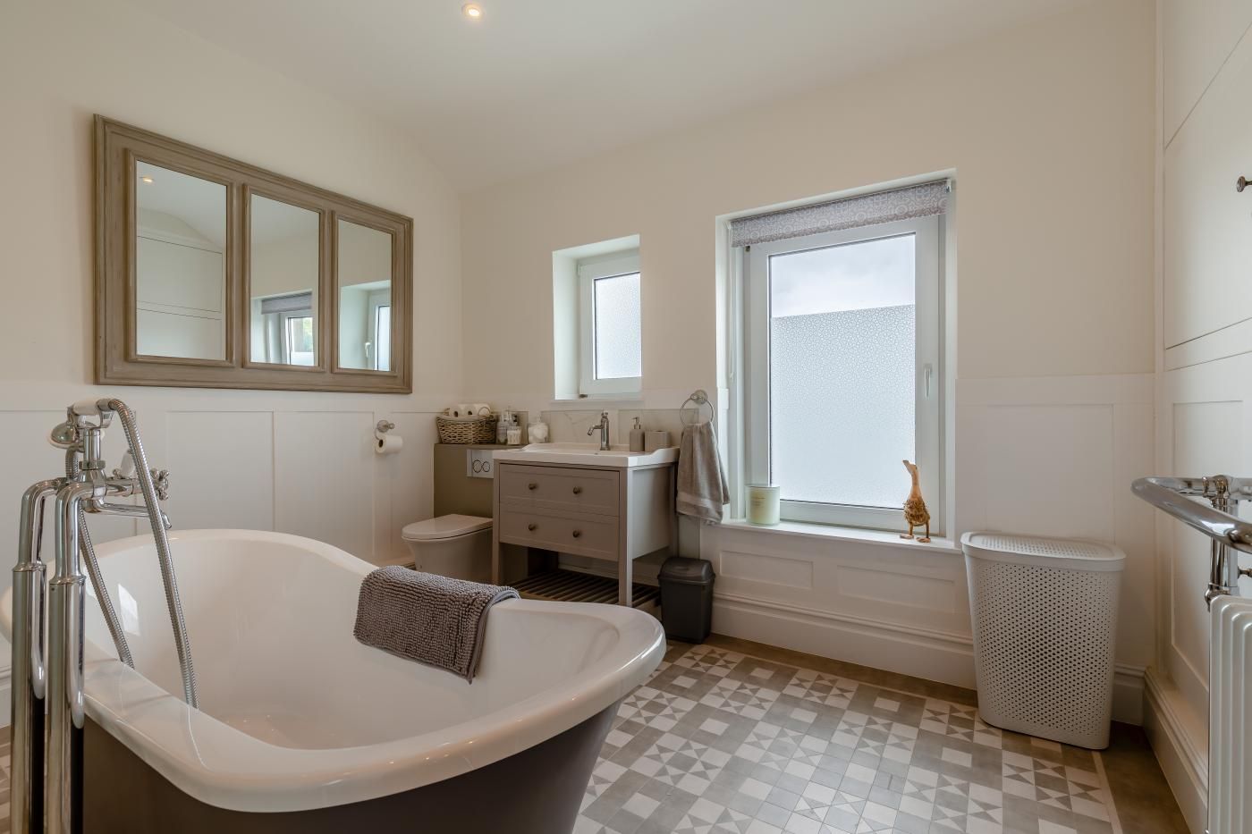 A bathroom with a freestanding bathtub, a vanity with a mirror, a window, and a radiator.