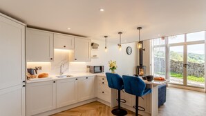 A modern kitchen with white cabinets, a herringbone wood floor, a built-in stove, and a large window offering a view of the countryside. - 1 Bed in Low Row (oc-c43317) (Low Row)