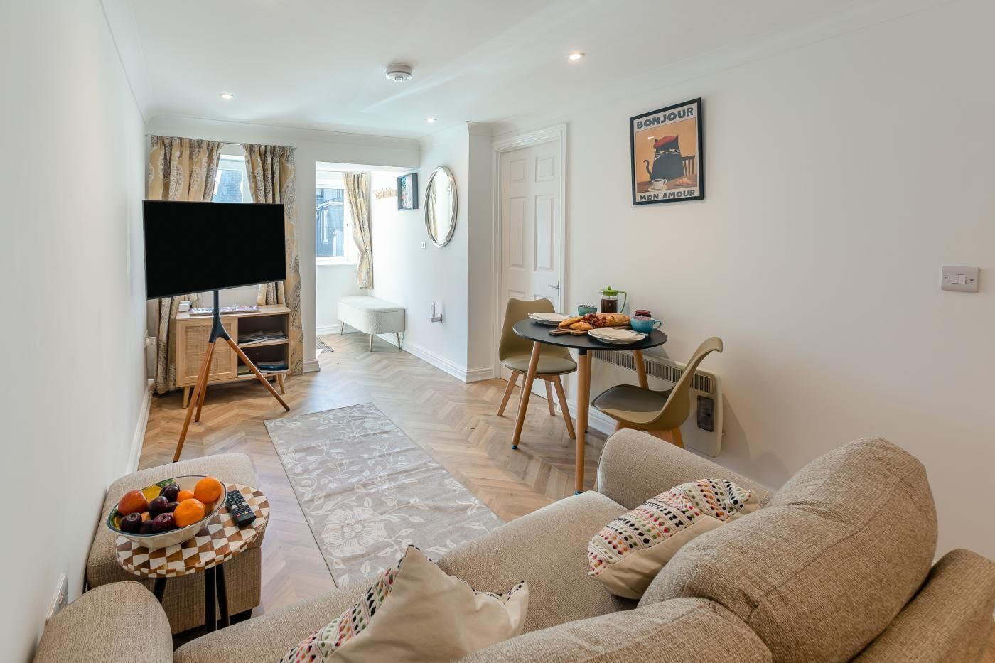 A living room with a sofa, a coffee table with fruit, a TV, and a dining area with chairs and a table.