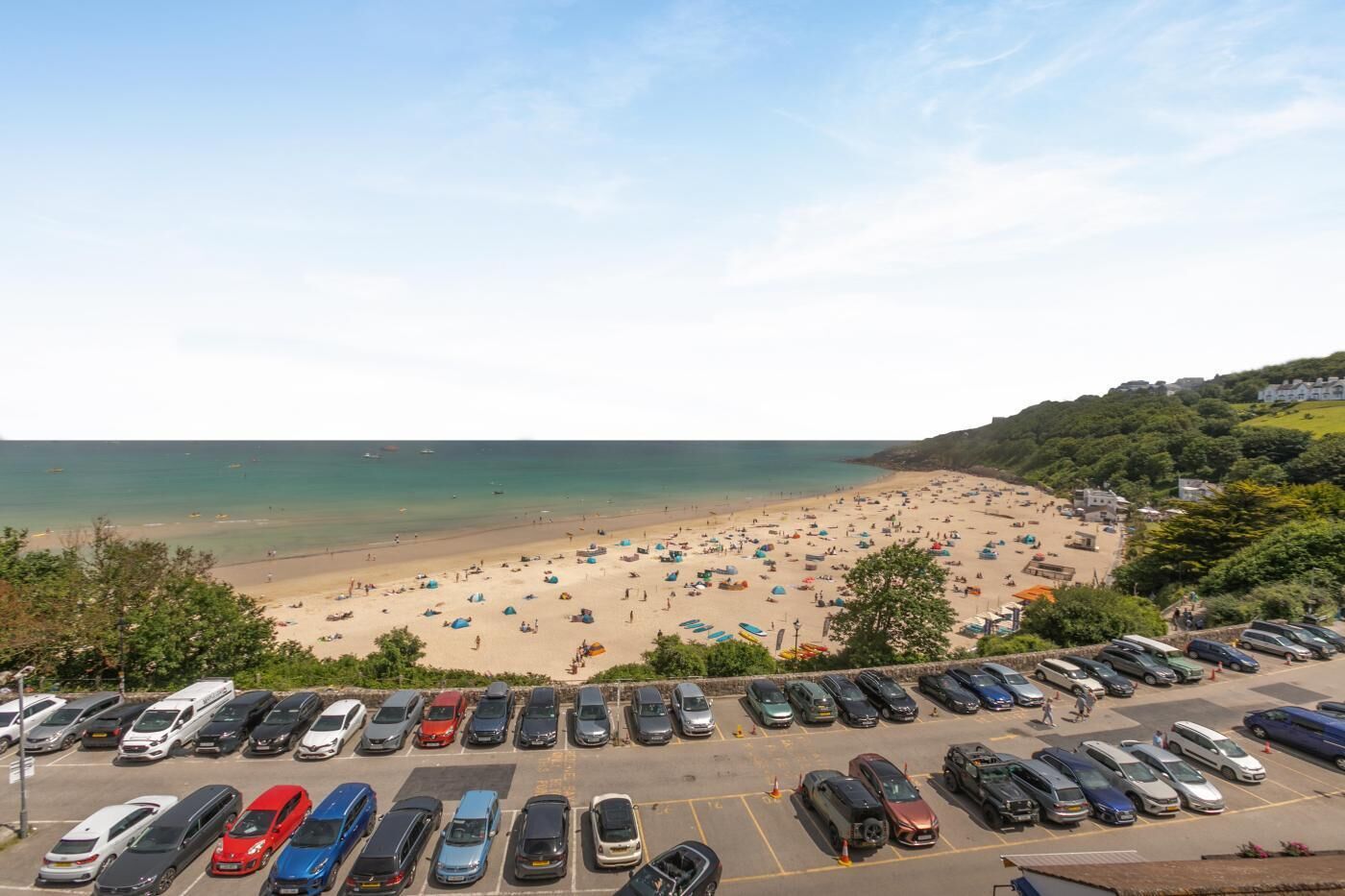 A beach with a parking lot in the foreground and a view of the sea.