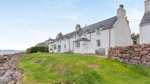 A row of white houses with grey roofs, a stone wall, and a grassy area in front. - 2 Bed in Strath (oc-s44223) (Gairloch)