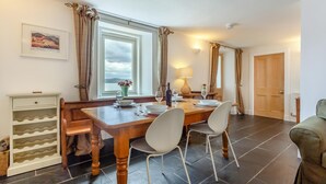 A dining area with a wooden table, white chairs, a wine bottle, and a lamp. - 2 Bed in Strath (oc-s44223) (Gairloch)