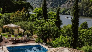 Una piscina con sillas de descanso y una mesa, rodeada de vegetación y vistas a colinas.
