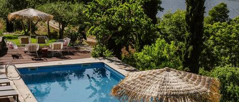 A swimming pool with lounge chairs and a table, surrounded by greenery and a view of hills.