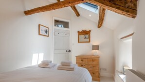 Une chambre à coucher avec un lit, une commode en bois, une porte et un puits de lumière.