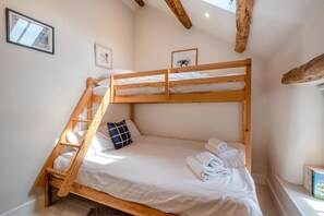 Ein Stockbett mit weißer Bettwäsche und einem blauen Kopfkissen, ein gerahmtes Bild an der Wand und ein Fenster mit Blick.