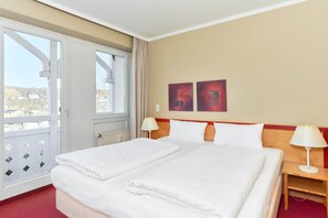 A hotel room with a large bed, two bedside tables with lamps, a window with curtains, and two wall-mounted artworks. - Ferienwohnung mit Badewanne in Sellin (Sellin)