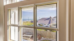 Ein Fenster mit Blick auf ein Haus an der Küste, eine Holzterrasse und eine Rasenfläche.