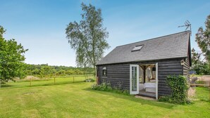 Ein kleines Holzhaus mit einer offenen Tür, einem eingezäunten Garten und blauem Himmel.