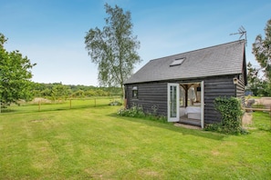 A small wooden house with a single open door, a fenced yard, and a clear sky.