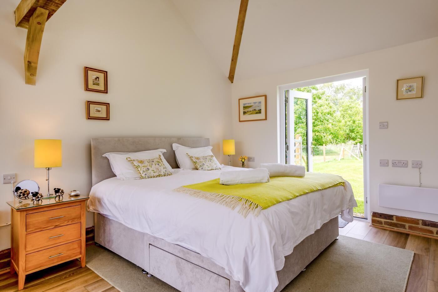 A bedroom with a bed, bedside lamps, a dresser, and a door leading to a garden.