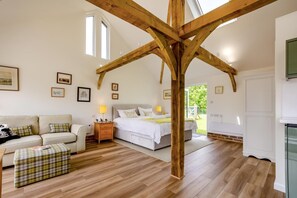 A bedroom with a wooden ceiling structure, a bed, a bedside table, a nightstand, a sofa, a bench, and framed pictures on the wall.
