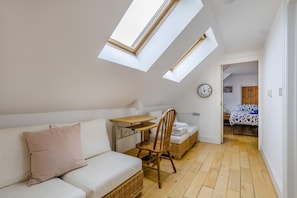 A compact room with a skylight, a sofa, a small table, a chair, and a bed.