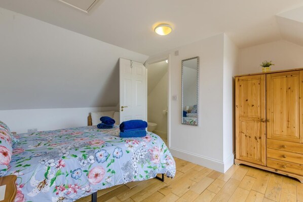 A bedroom with a bed, a wooden wardrobe, a mirror, and a door leading to another room.