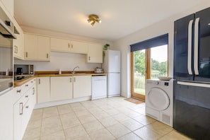 A modern kitchen with white cabinets, a dishwasher, a washing machine, and a black refrigerator.