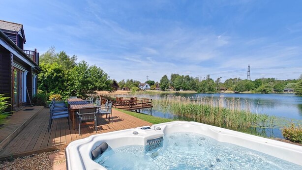 Ein Whirlpool mit Holzterrasse und Stühlen, ein Teich und ein Haus im Hintergrund.