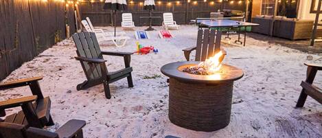 A sandy outdoor area with a fire pit, lounge chairs, and a ping pong table.