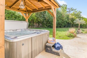 Ett bubbelbad under en träpergola i en vackert anlagd trädgård.