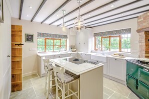 A kitchen with a central island, wooden shelving, and a green stove. - 4 Bed in Radford (oc-r33951) (Rous Lench)
