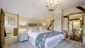 Een slaapkamer met een bed, nachtkastjes, een kroonluchter, een trap en een spiegel.