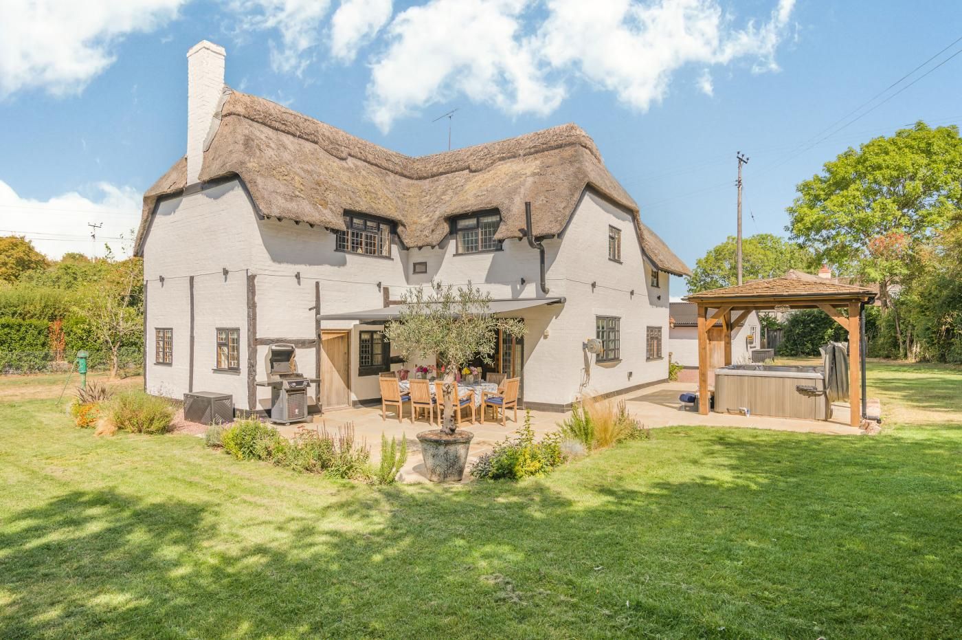 A white house with a thatched roof, a patio with outdoor furniture, and a wooden pergola.