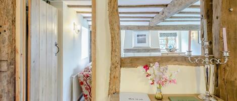 A rustic interior with exposed wooden beams, a wooden desk with a vase of flowers, and a framed picture on the wall.