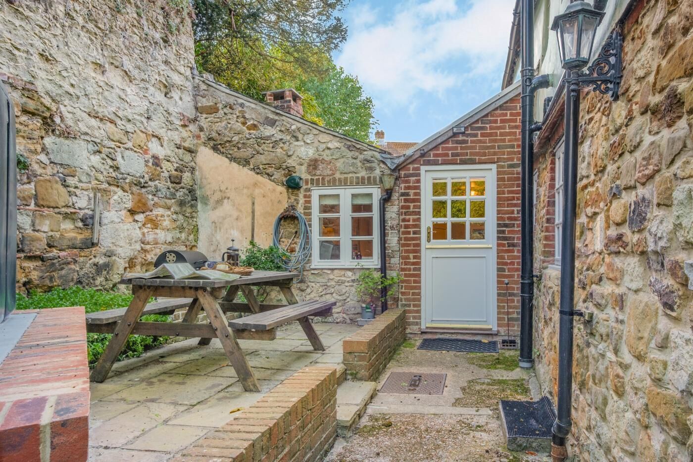 A stone wall, a wooden picnic table, a white door with glass panels, and a brick pathway.