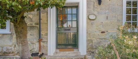 A stone building with a green door, a small porch, and a tree.