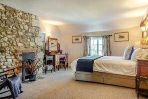 A bedroom with a stone wall, a desk with a chair, a bed, and a window with curtains. - 4 Bed in Shorwell (oc-w42664) (Shorwell)