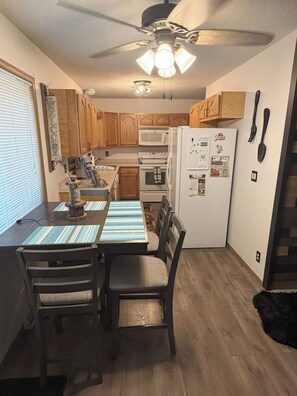 A compact kitchen with wooden cabinets, a microwave, a refrigerator, and a dining table with chairs. - Secluded Woodland Retreat for 6 Near Wisconsin Dells, Lakes & ATV Trails (New Lisbon)