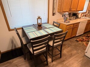 A dining area with a table, chairs, a lantern, and a kitchen in the background. - Secluded Woodland Retreat for 6 Near Wisconsin Dells, Lakes & ATV Trails (New Lisbon)